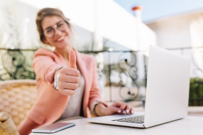 cute-young-woman-student-business-lady-showing-thumbs-up-well-done-sitting-outdoor-cafe-terrace-with-laptop-wearing-pink-smart-clothes